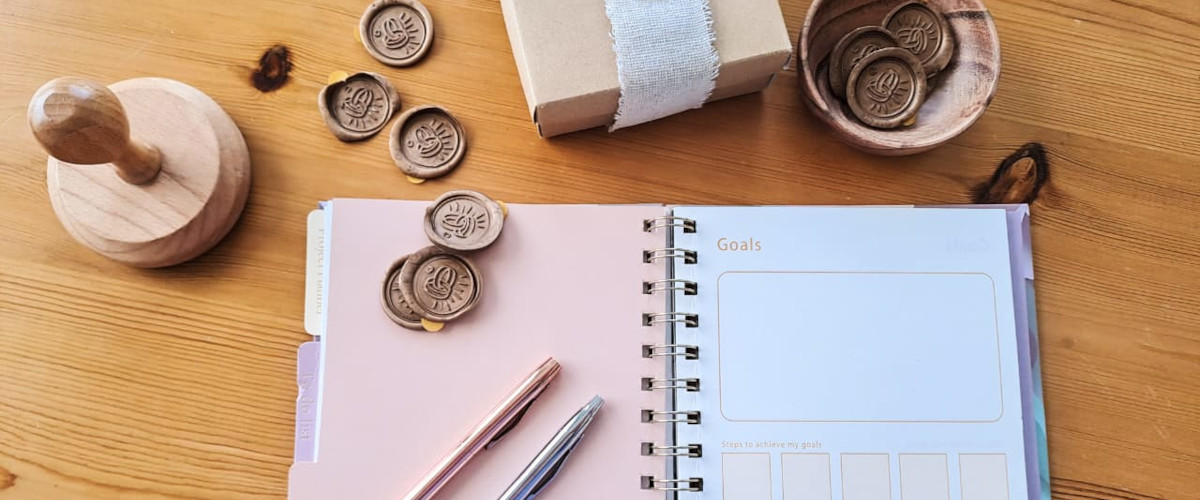 A notepad, pen, and wax seal elegantly arranged on a wooden table, symbolizing wedding planning in Mykonos.