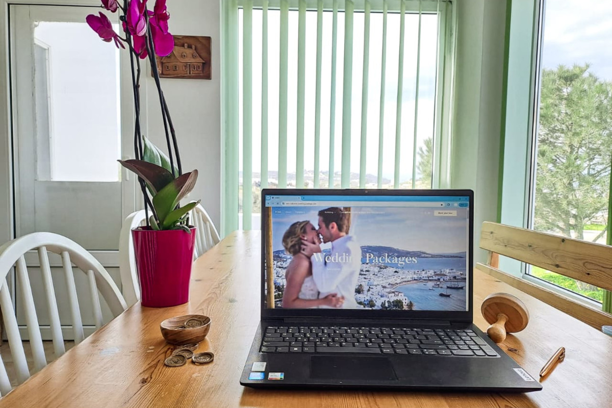 A laptop on a table beside a vase of flowers, symbolizing Mykonos wedding coordination and planning.