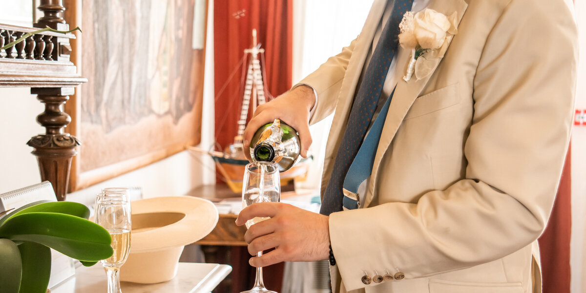 a groom pooring champaign in a glss at Mykonos Town hall at this Mykonos wedding package