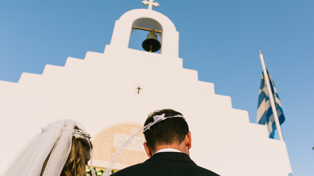 A wedding photographer in Mykonos captures a couple's special moment against the backdrop of the iconic white traditional chapel.